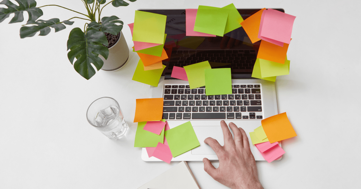 Computador com post-its coloridos ao redor do teclado, mesa organizada com planta e copo, representando estratégia prática para TDAH e procrastinação