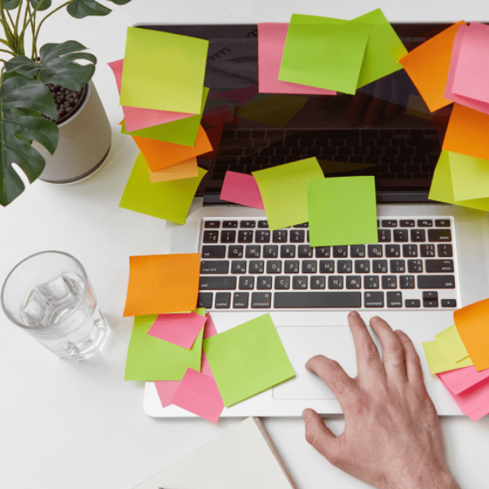 Computador com post-its coloridos ao redor do teclado, mesa organizada com planta e copo, representando estratégia prática para TDAH e procrastinação